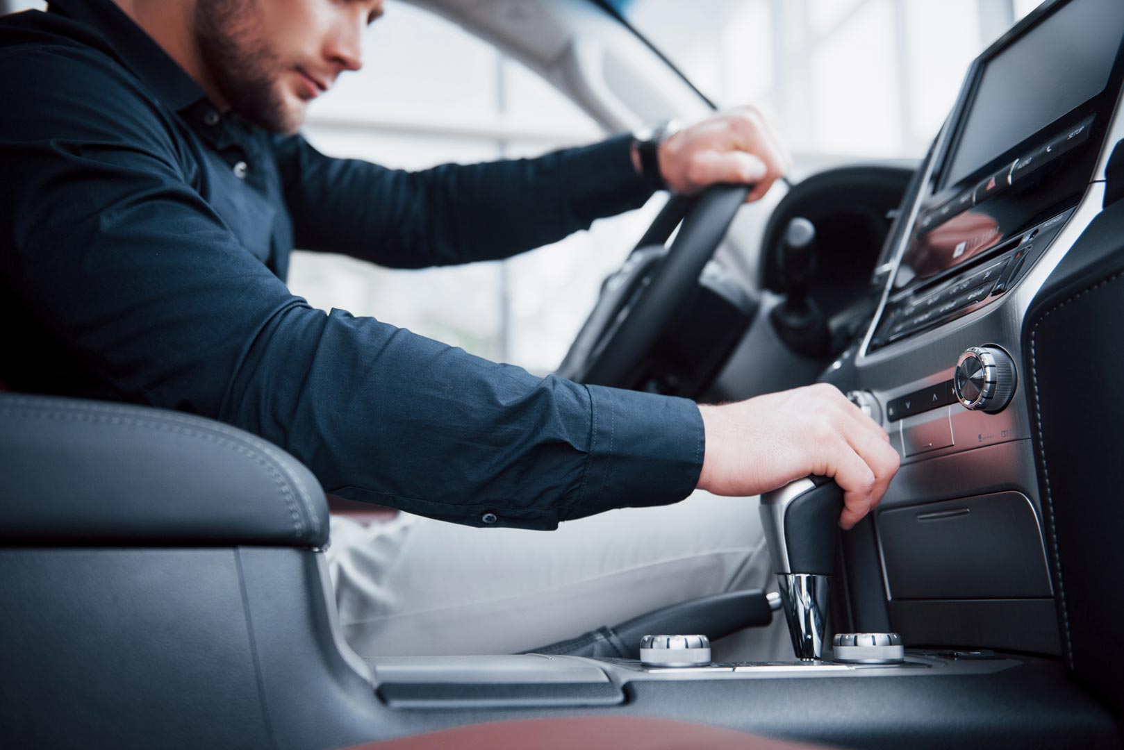 A man sitting in the drivers seat looking at his transmission gear shifter.